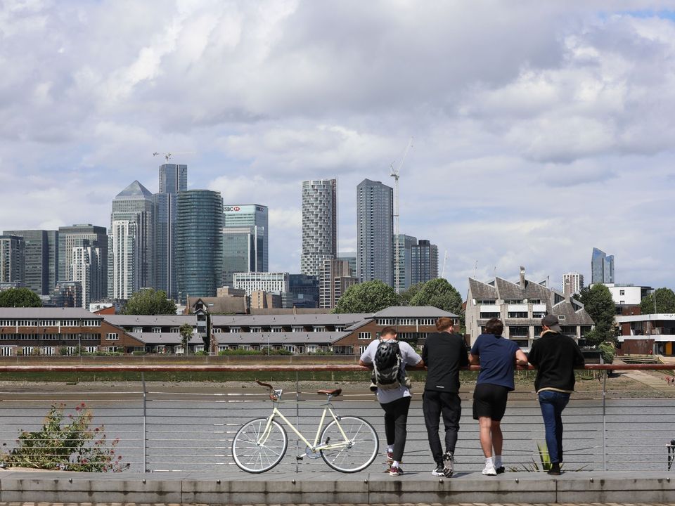 People walking by the river with Canary Wharf's towers behind