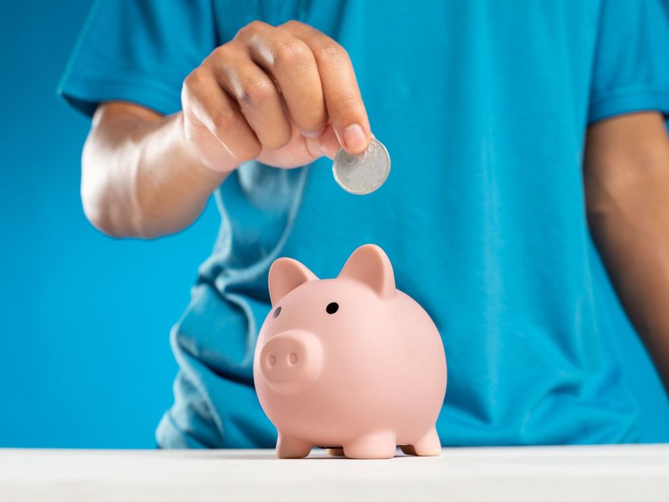 A hand dropping a coin into a pink piggy bank