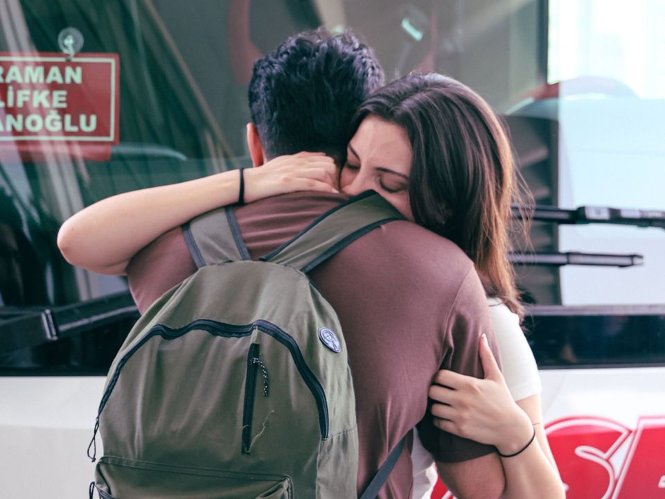 A young couple hugging goodbye with a backpack on