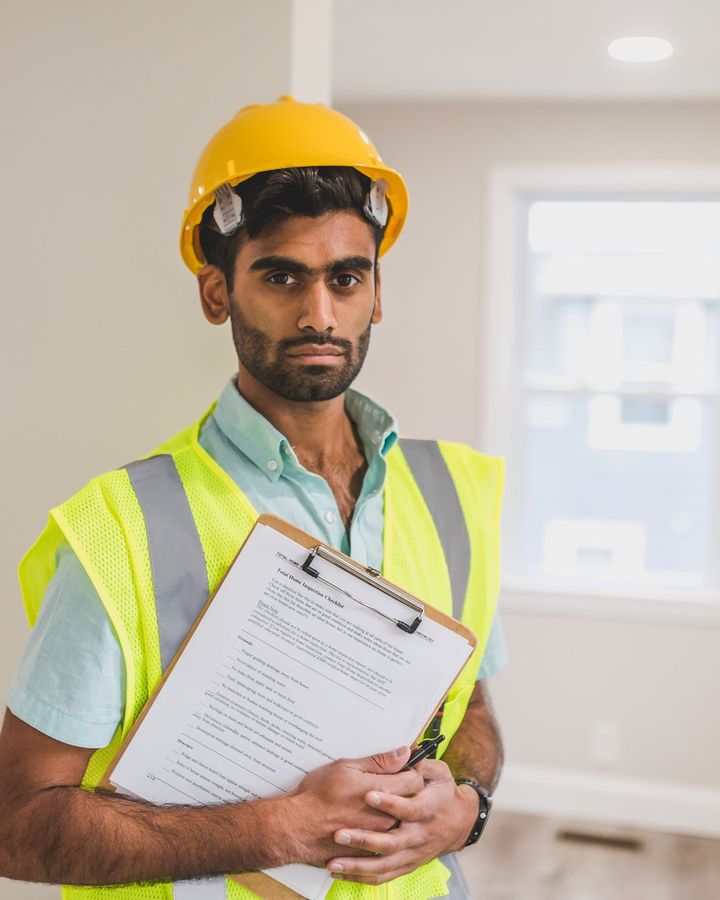 A young engineer in a hard hat and safety vest holding a clipboard