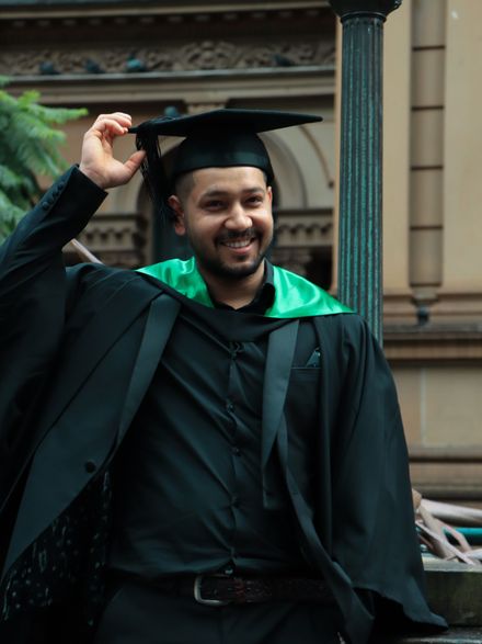 Excited university graduate in cap and gown celebrating outdoors in Sydney, Australia.