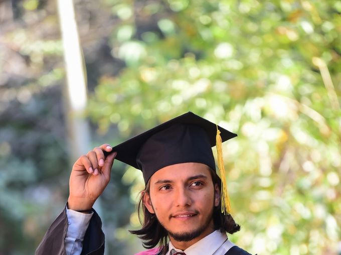 A young man in graduation robes celebrating outdoors
