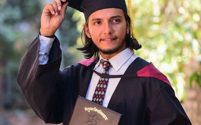 A young man in graduation robes celebrating outdoors