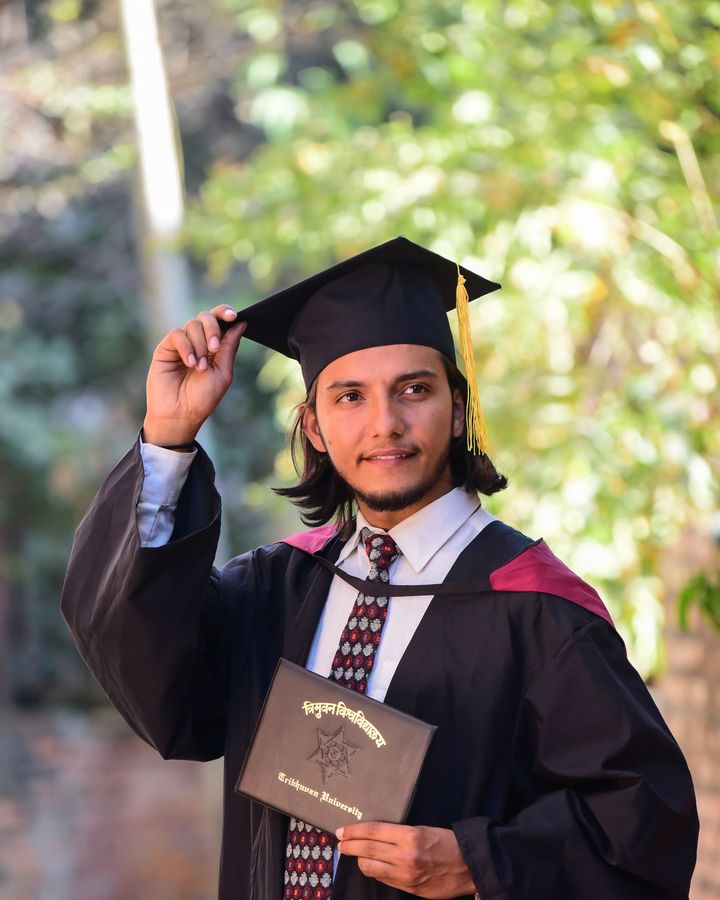 A young man in graduation robes celebrating outdoors
