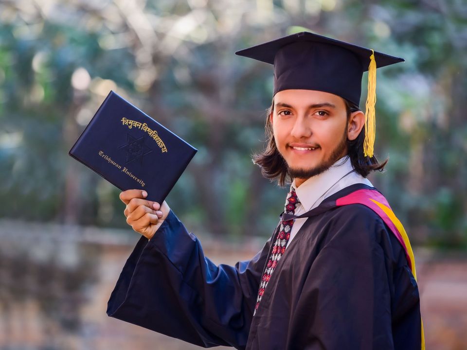 A graduate in a cap and gown holding up his diploma