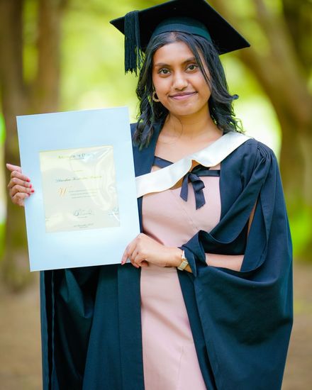 A graduate in cap and gown holding up her certificate outdoors