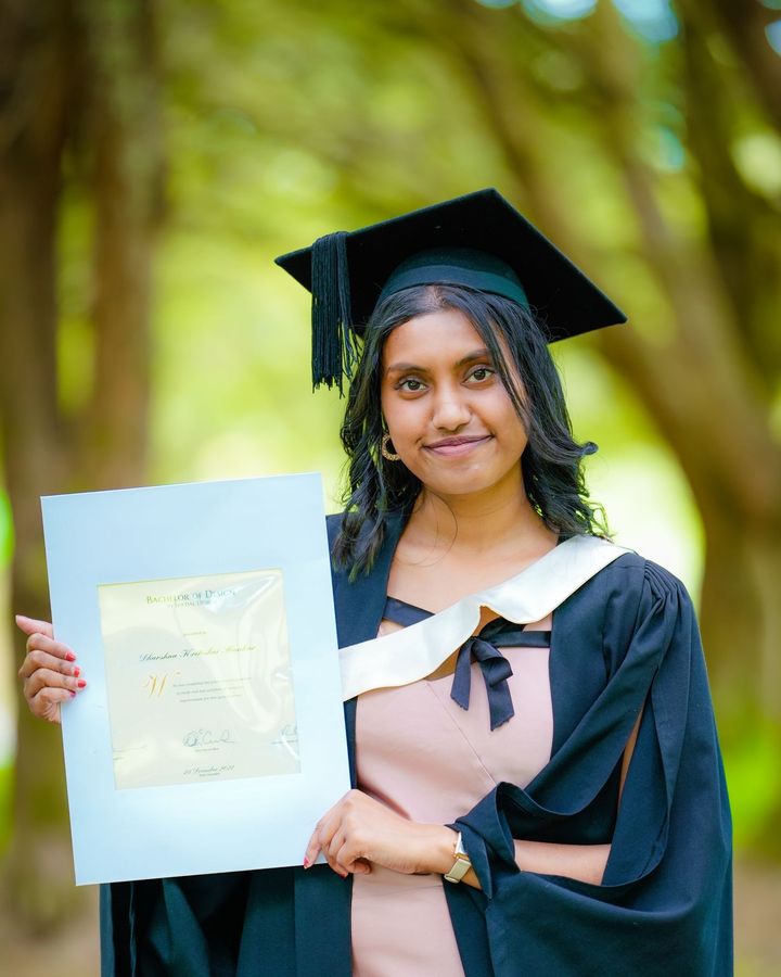 A graduate in cap and gown holding up her certificate outdoors