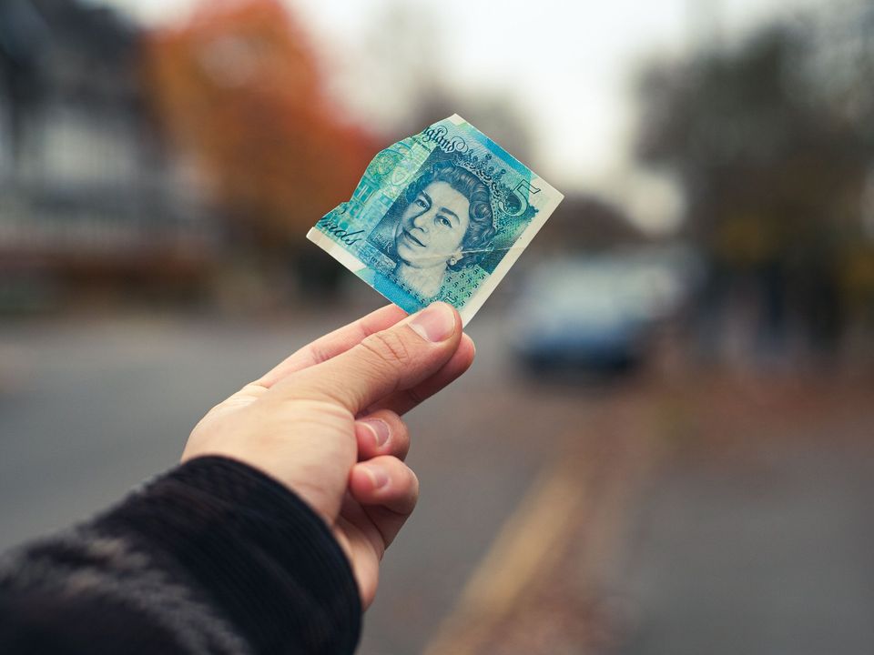 A hand holding a British pound note on a city street