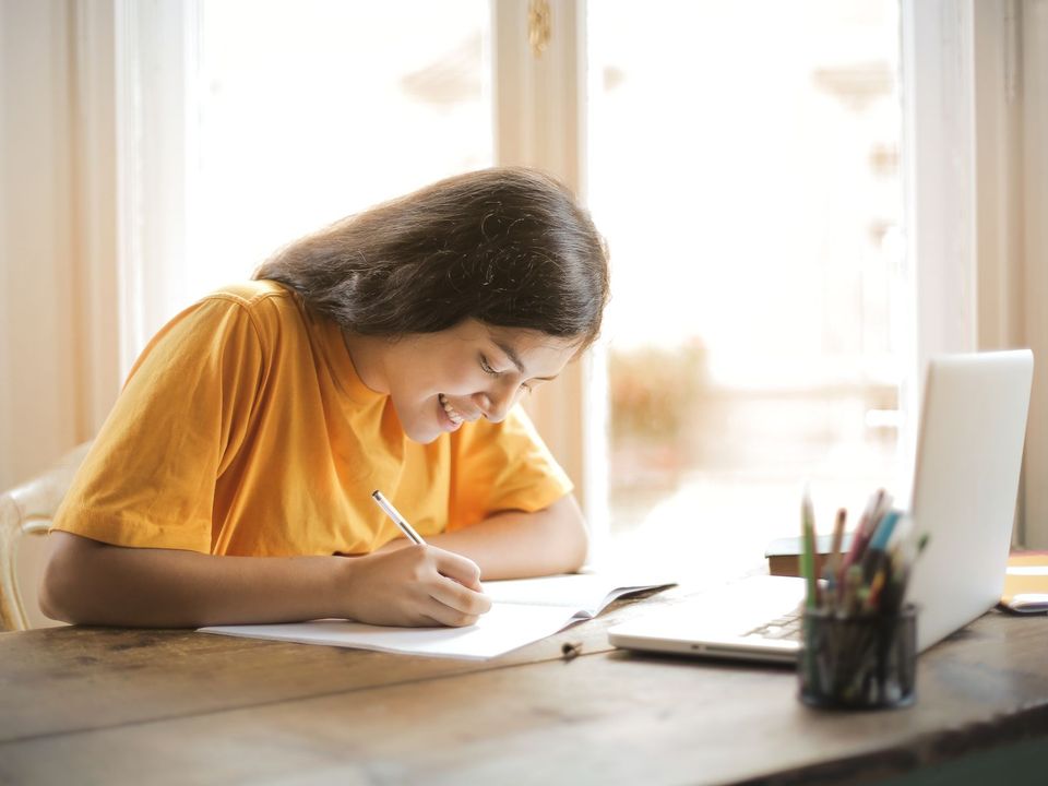 Young woman studying with a laptop and notepad at home, smiling.