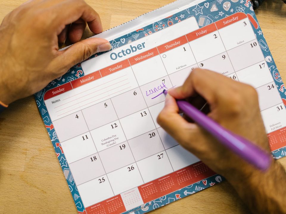 A hand marking dates on a monthly calendar