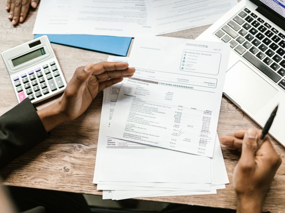 Hands working through bank documents with a calculator and a laptop