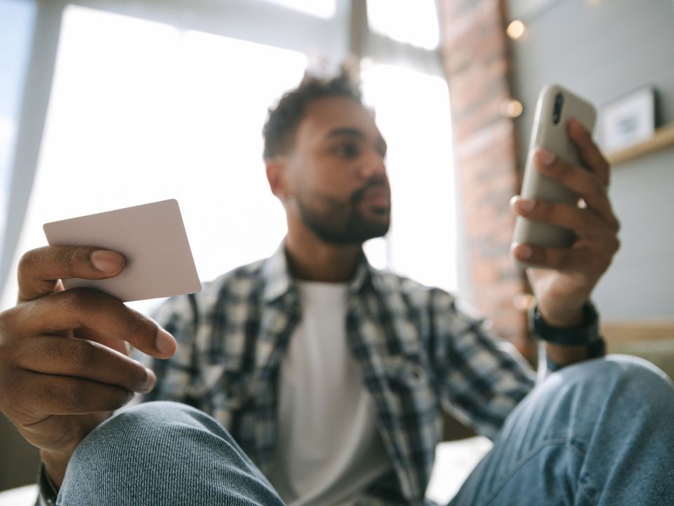 A young man holding a bank card and his phone