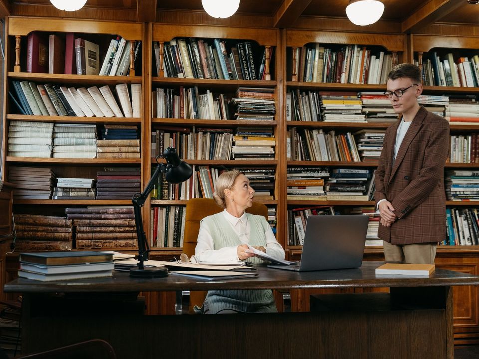 A professor at her desk in a library office with a student