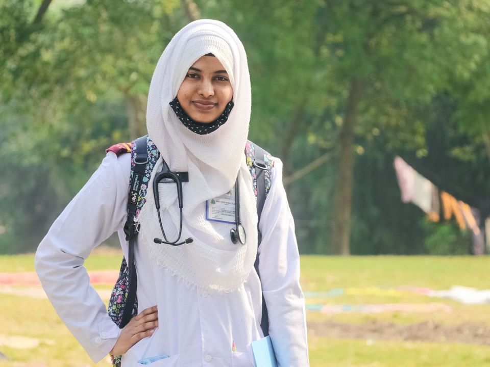 Smiling female doctor with a stethoscope standing outdoors in Dhaka.