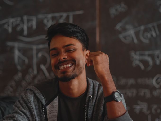 A smiling young man at a desk in front of a chalkboard