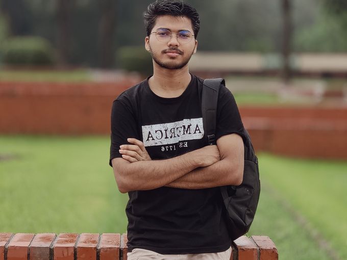 A young man leaning on a brick wall on a college lawn