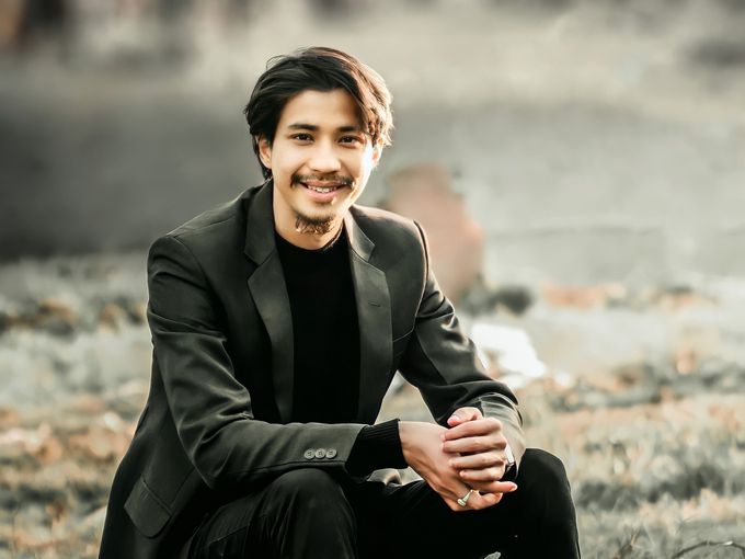 A smiling young man in a blazer sitting outdoors