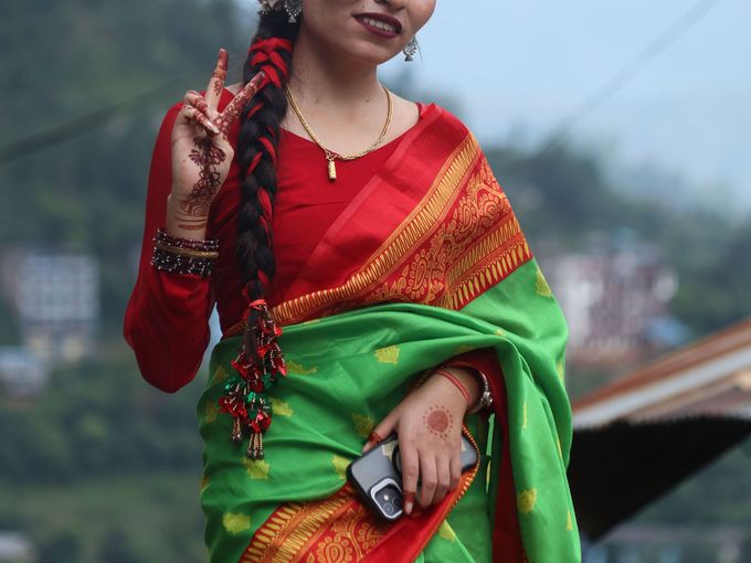 A smiling young woman in a green and red sari on a hillside