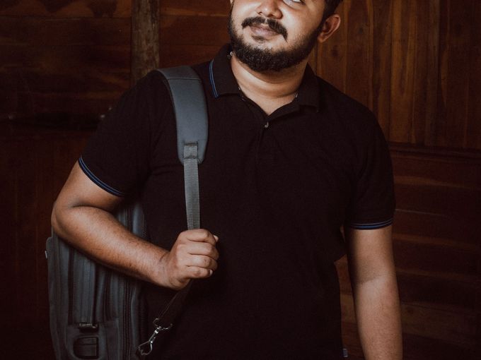 A smiling young man with a backpack against a dark wall
