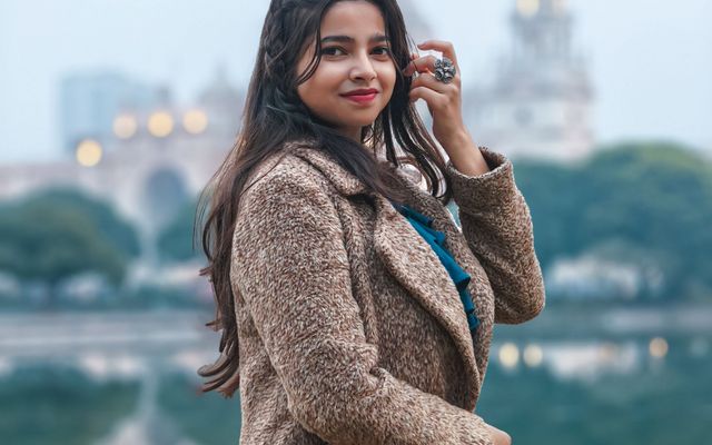A student in a camel coat by a lake in a European city
