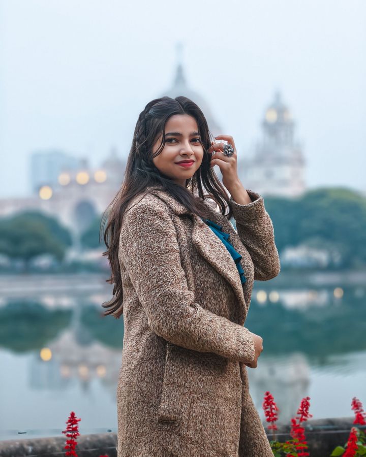 A student in a camel coat by a lake in a European city