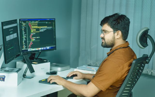 A student writing code on two monitors