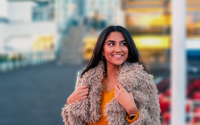 A smiling student in a winter coat on a city street