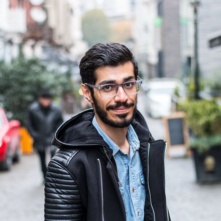A smiling student in a black jacket on a European street