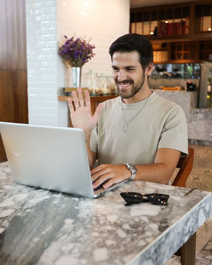 A student smiling while working on a laptop in a cafe