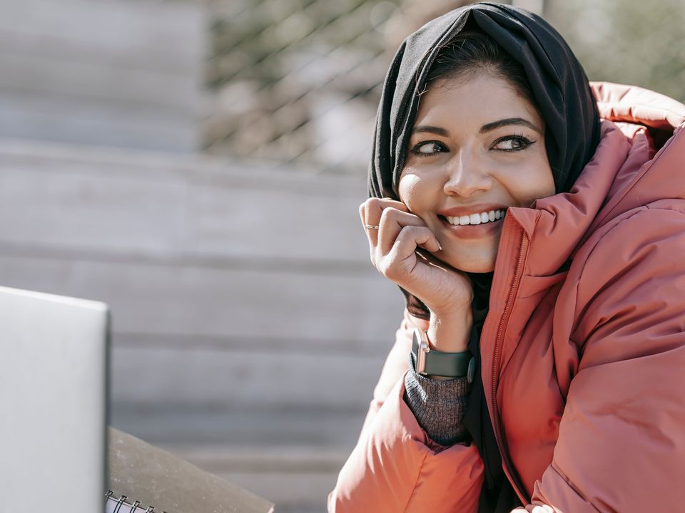 A student in a winter jacket smiling at her laptop outdoors