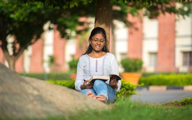 A student reading on the lawn of a brick university building