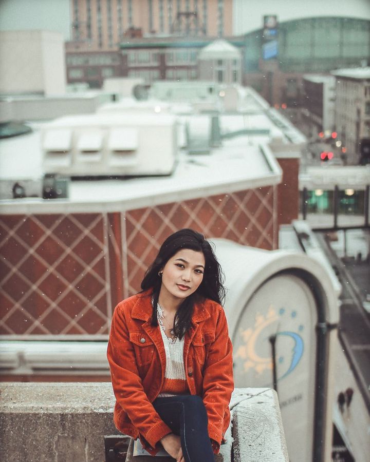 A student in a red jacket sitting on a railing above a city