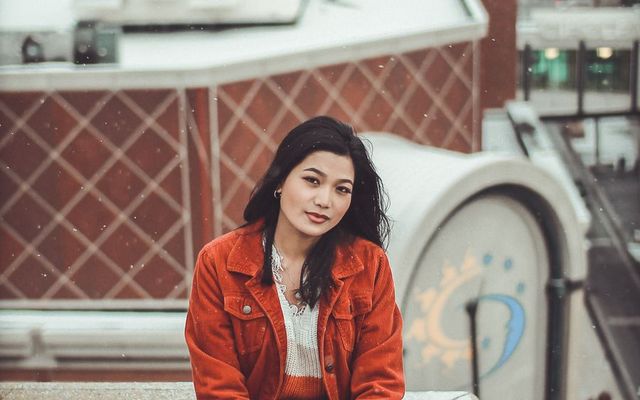 A student in a red jacket sitting on a railing above a city