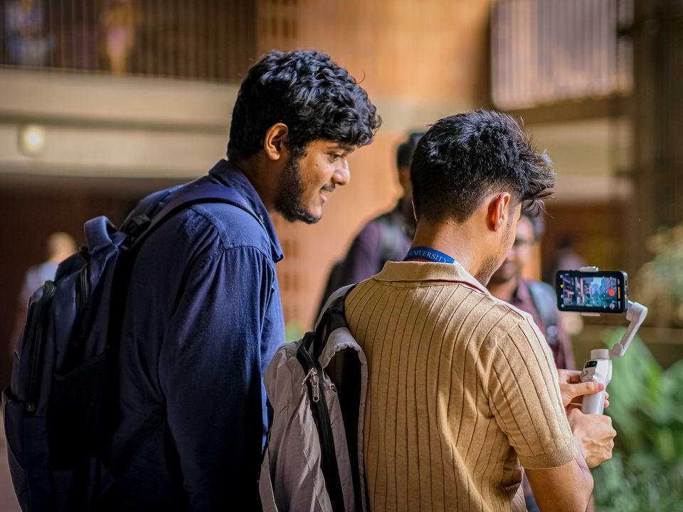 Two students with backpacks looking at a phone in a campus corridor