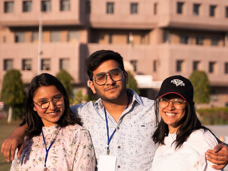 Three students with lanyards smiling outside a university building