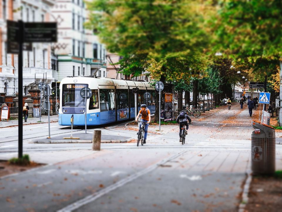 A tree-lined street in Gothenburg with a blue tram and cyclists