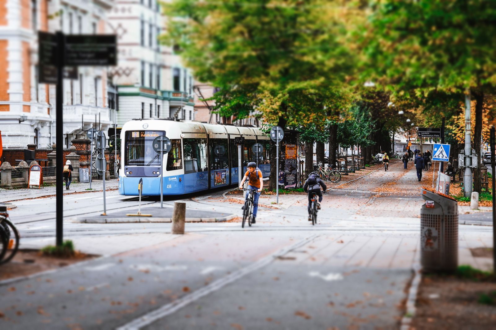 A tree-lined street in Gothenburg with a blue tram and cyclists