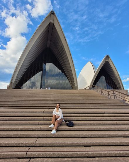 A student sitting on the steps of the Sydney Opera House under a clear sky