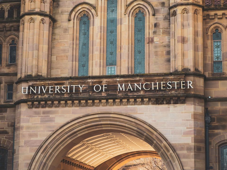 The arched entrance of a red-brick university building in Manchester