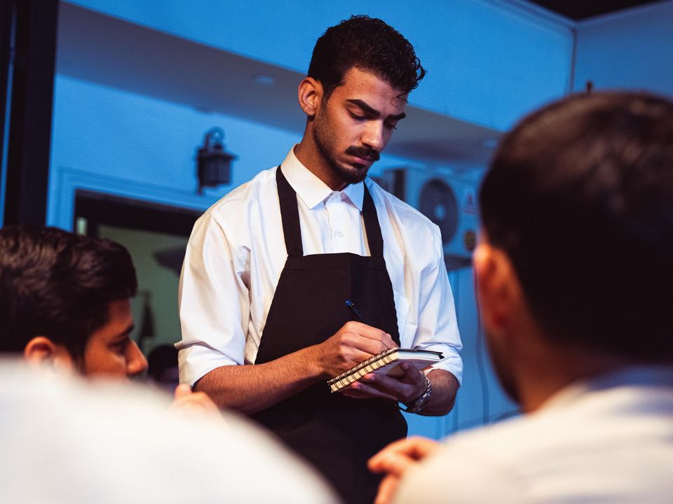 A young waiter taking an order at a restaurant table