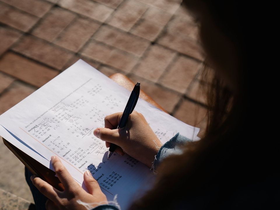 A student's hand writing answers on an exam sheet